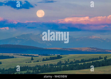 full moon setting above peaks of the flint creek range and foothills near avon, montana Stock Photo