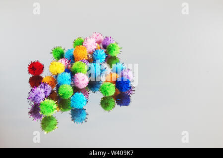 Colored beautiful pompons on a gray background. Assortment of pompons on the mirror surface. Stock Photo