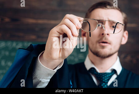 Let me see. Teacher formal wear and glasses looks concentrated, chalkboard background. Chalkboard full of math formulas. Man in end of lesson checking Stock Photo