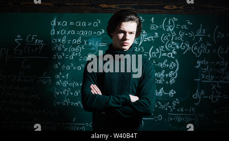 Modern teacher hipster writing on big blackboard with math formula. High school college students studying and reading together in class education conc Stock Photo