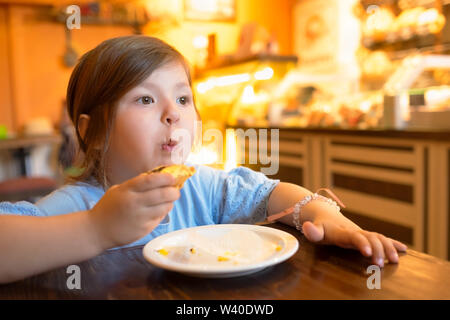 Cheerful nice little girl sitting at the table while eating sweet cake Stock Photo