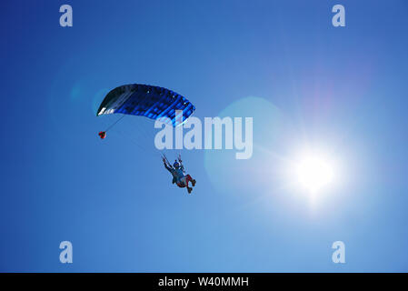 Skydiver under a blue little canopy of a parachute on the background a sun and a blue sky, close-up. Silhouette of the skydiver with parachute against Stock Photo