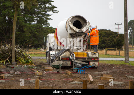 Annat, Canterbury, New Zealand, July 19 2019: Builders wheelbarrow wet cement from a concrete mixer truck for foundation piles on a rural building sit Stock Photo