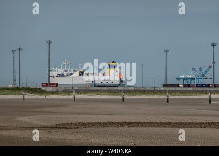 Zeebrugge, Flanders, Belgium -  June 18, 2019: Ferry and container ship with Container cranes in port of Zeebrugge, as seen from beach in Knokke-Heist Stock Photo