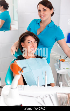 The dentist and her happy patient look at the camera and smile. Reception at the dentist, healthy teeth, happy patient, beautiful teeth. Stock Photo