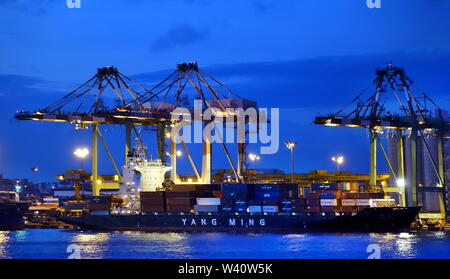 KAOHSIUNG, TAIWAN -- JUNE 2, 2019: Containers are being loaded onto ships in Kaohsiung Port at dusk Stock Photo