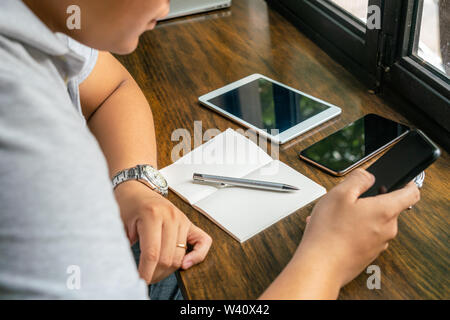Close up of Asian businessman using cellphone on rustic table Stock Photo