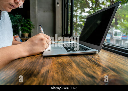 Asian man sitting in front of laptop and writing notes  Stock Photo