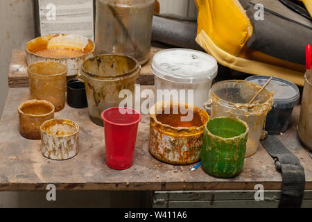 Multi-colored cans and containers with old dried paint and glue of yellow color on the table in the workshop for work with textiles and fabrics. Indus Stock Photo