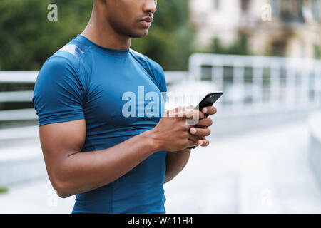 Cropped image of handsome young strong sports man outdoors using mobile phone chatting. Stock Photo