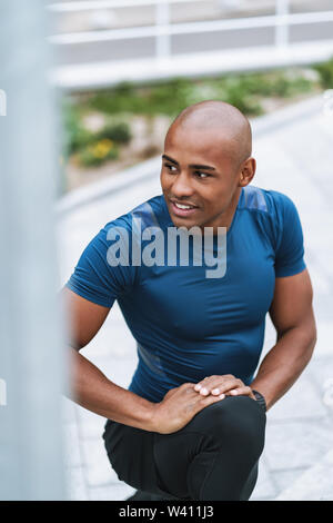 Smiling handsome fit african fitness man doing stretching exercises on stairs outdoors Stock Photo