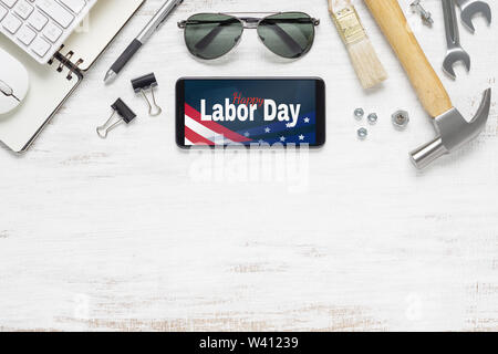 Table top view of labor day abstract background concept. Flat lay mockup smartphone with Happy Labor Day USA Holiday and essential worker tools on gru Stock Photo