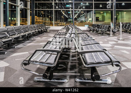 Empty black seats at airport gate terminal at night with reflections in large windows Stock Photo