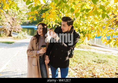 Image of a happy young beautiful loving couple posing walking outdoors in park nature pointing. Stock Photo