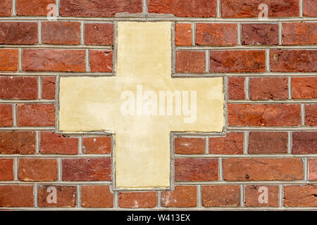 Red brick wall with white-yellowish cross sign background Stock Photo