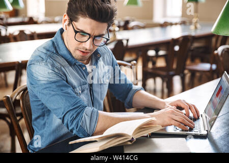 Confident man student wearing earphones studying at the library with laptop and books Stock Photo