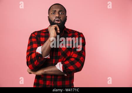 Portrait of a pensive african man wearing plaid shirt standing isolated over pink background, thinking Stock Photo