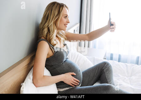Young blond pregnant woman relaxing at home sitting on rocking