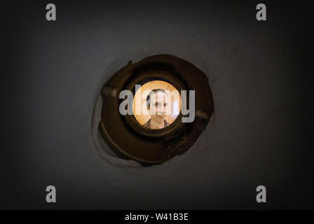 Woman seen out of focus through the old dirty peephole of the front door of a dark apartment Stock Photo