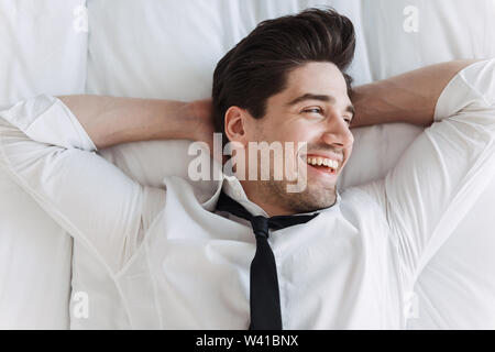 Photo from top of european smiling businessman wearing formal clothes lying on bed in hotel apartment Stock Photo