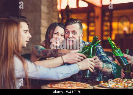 Friends having a drinks in a bar, They are sitting at a wooden table with beers and pizza. Stock Photo