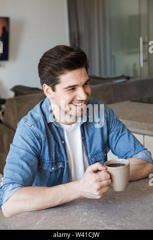 Attractive young man sitting at the kitchen at home, drinking coffee Stock Photo