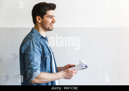 Attractive young man standing at the kitchen at home, holding clipboard, working Stock Photo