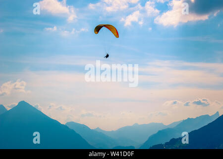 Paragliders flying over mountains in Interlaken, Switzerland. Silhouette of Swiss Alps. Tandem paragliding. Dawning, sunset. Extreme sports. Adventure lifestyle. Adrenaline, risk concept. Stock Photo