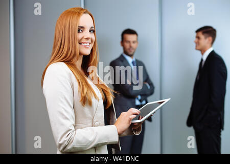 Beautiful business woman standing with digital tablet with business people in background Stock Photo
