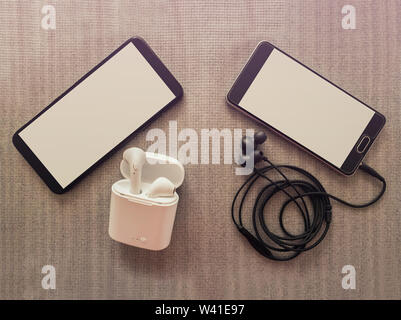 Comparison between two phones, one has 3.5mm jack wired headphones vs wireless earphones for music listening. Pros and cons, opposite contrary. Techno Stock Photo