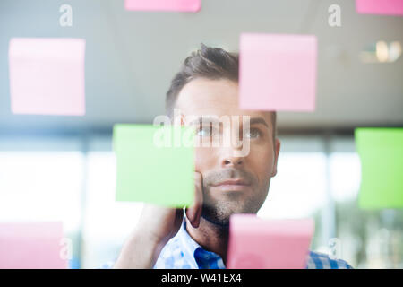 Portrait of handsome businessman looking at sticky notes on glass wall in modern office Stock Photo