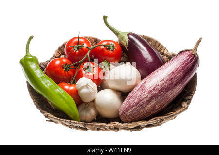 Fresh eggplants, tomatos, green pepper, onion and garlic placed in a wicker basket over white background Stock Photo