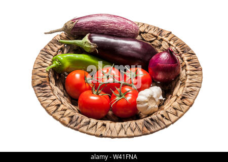 Fresh eggplants, tomatos, green pepper, onion and garlic placed in a wicker basket over white background Stock Photo