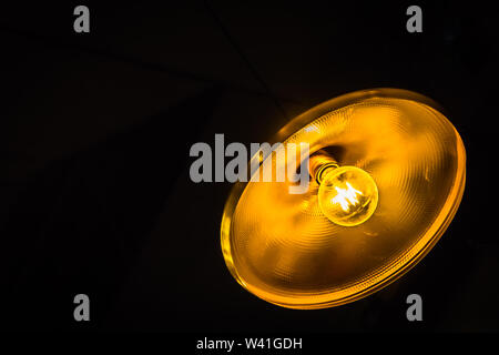 Lighted Incandescent bulb with round reflector against a dark background. Stock Photo
