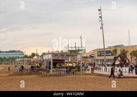 Barcelona, Spain- 09 November 2014: Restaurants and people on the most fashionable Barceloneta Beach. Modern building in the background. Stock Photo