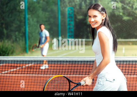 Dark-eyed wife smiling while playing tennis with husband Stock Photo