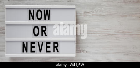 'Now or never' word on a lightbox on a white wooden background, top view. Copy space. Stock Photo