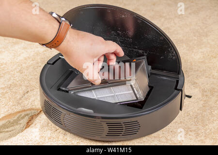 The hand pulls out a container of garbage from the robot vacuum cleaner Stock Photo