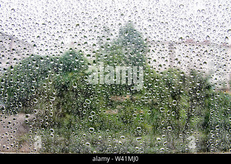 Raindrops on the window against the background of houses and trees Stock Photo