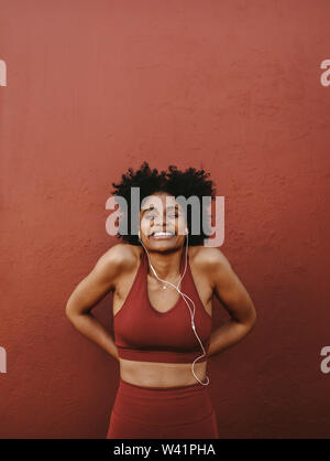 Healthy and fit woman standing by a wall and smiling. Female taking a rest after training session. Stock Photo