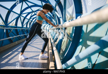 Fitness woman doing stretching with the support of bridge railing. Female athlete doing stretching exercises. Stock Photo
