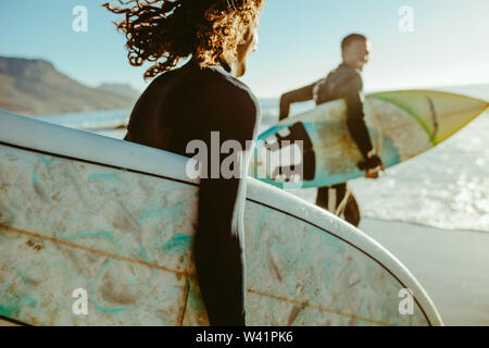 Two young men with surfboard going for surfing in the sea. Surfers carrying surfboards running on the beach. Stock Photo