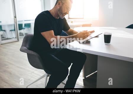 Male entrepreneur with digital tablet in office. Businessman using tablet pc while sitting at table in bright office space. Stock Photo