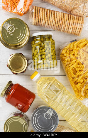 Various uncooked cereals, grains, pasta and canned food on a white wooden table. Flat lay. Stock Photo