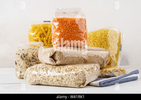 Various raw groats, cereal grains and pasta in transparent plastic bags on a kitchen table. Ingredients for cooking. Stock Photo