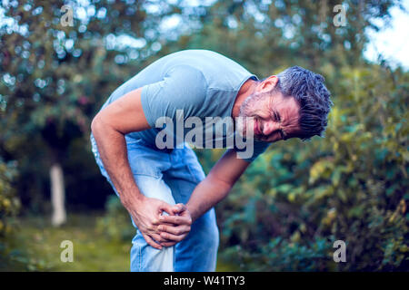 People, healthcare and problem concept - close up of an unhappy man suffering from pain in leg or knee outdoor Stock Photo