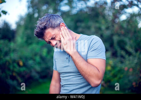Unhappy man having ear pain touching his painful head outdoor Stock Photo