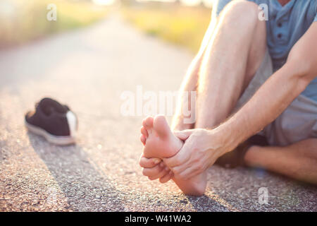 Healthcare, medicine and people concept. Unhappy man sitting on the ground suffering from pain in feet Stock Photo