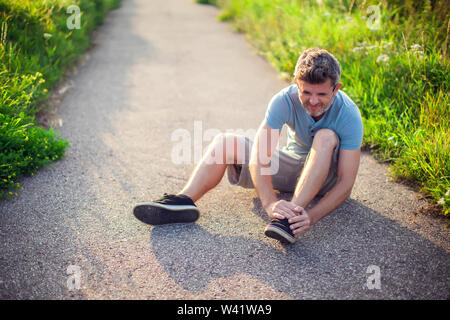 Healthcare, medicine and people concept. Unhappy man sitting on the ground suffering from pain in feet Stock Photo