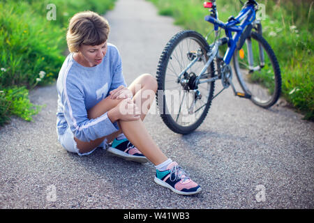 Woman with short hair with pain in knee joints after biking on bicycle. Sport, healthcare and people concept Stock Photo